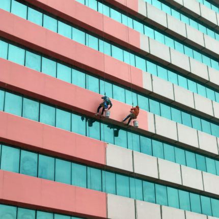 Two workers cleaning the windows of a high-rise building in Thailand, showcasing urban architecture.