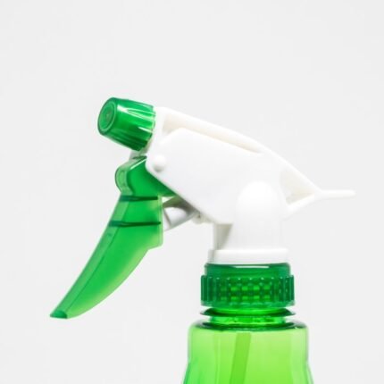 Close-up of a green plastic spray bottle nozzle with a white handle on a light background.