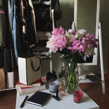 Beautiful pink peonies in a vase add a touch of elegance to a stylish room with clothing rack and makeup items.