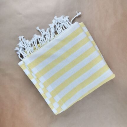A yellow and white striped beach towel neatly folded on a brown surface, perfect for summer vacations.
