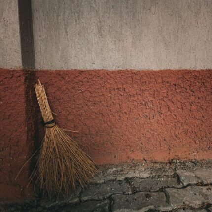 A rustic broom leans against a textured wall, showcasing simple, traditional tools.