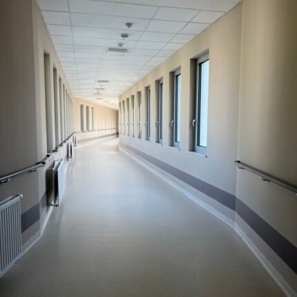 A modern, empty hospital corridor with large windows and handrails, well-lit and inviting.