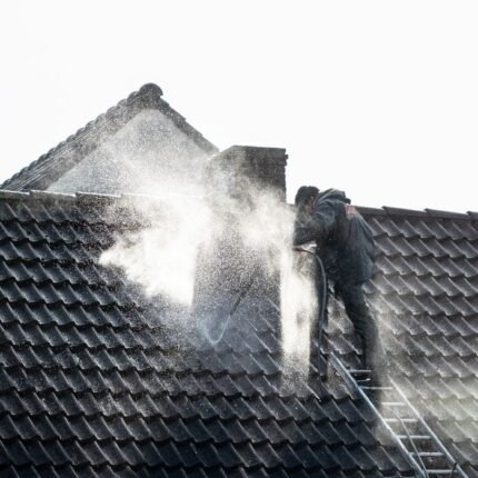Worker power washing roof tiles, removing grime and buildup.